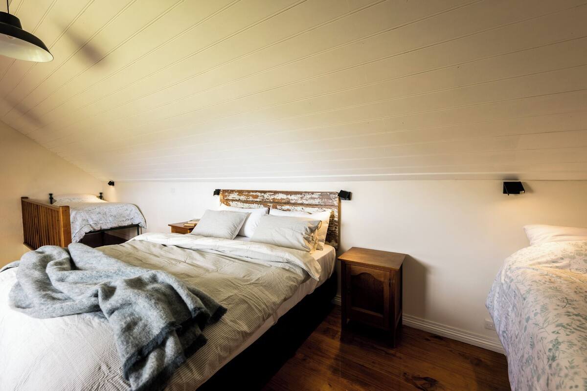 A bedroom with a sloped ceiling, a bed with a wooden headboard, a bedside table, and a nightstand.