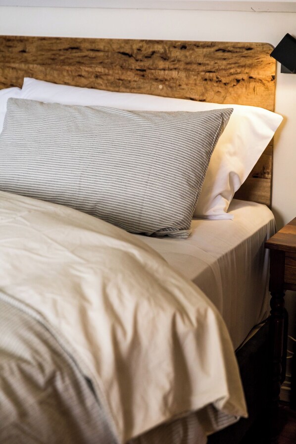 A bed with a wooden headboard, a striped pillow, and a plain pillow. - Daisy Bank Cottages (Richmond)