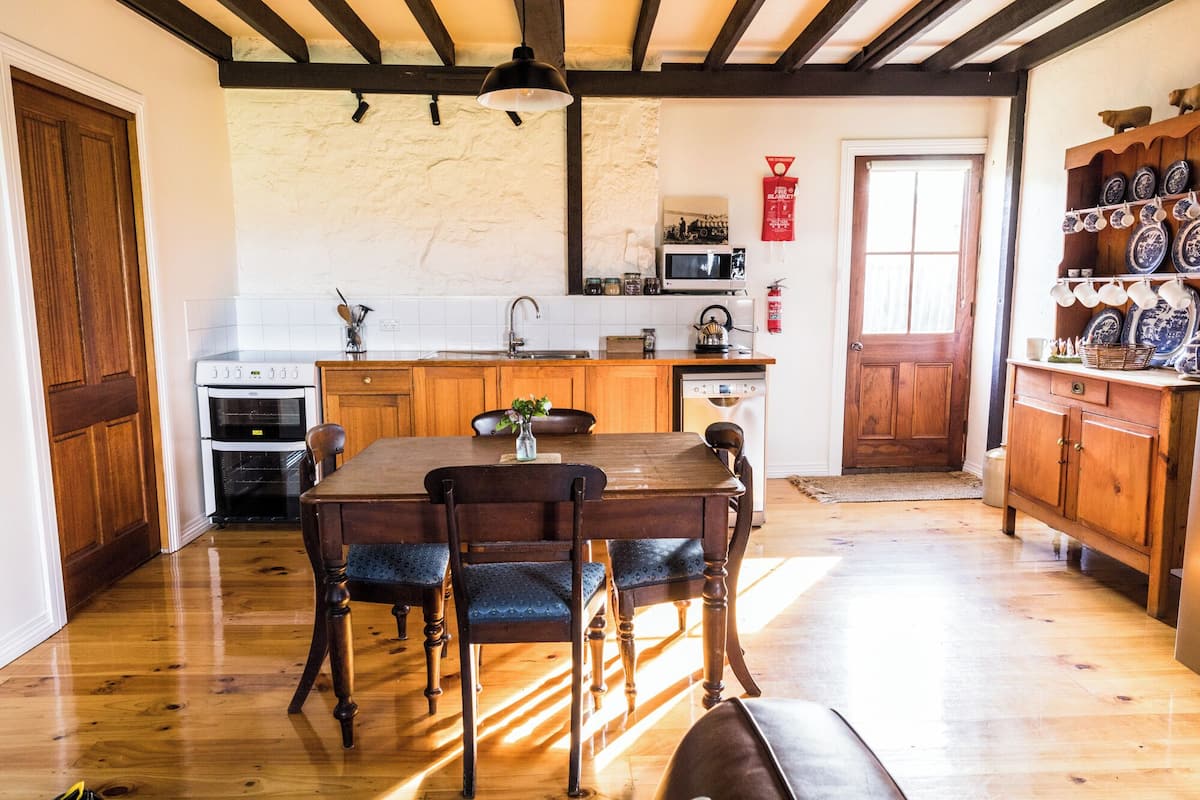 A kitchen with wooden cabinets, a dining table with chairs, a microwave, and a sink.