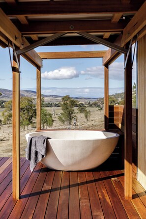 A large freestanding bathtub in an outdoor wooden structure with a view of a rural landscape. - Daisy Bank Cottages (Richmond)