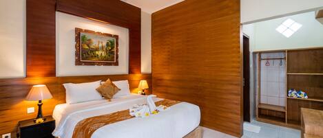 Habitación de hotel con una cama grande, cabecera de madera, un cuadro en la pared, una mesita de noche con lámpara y un armario de madera.