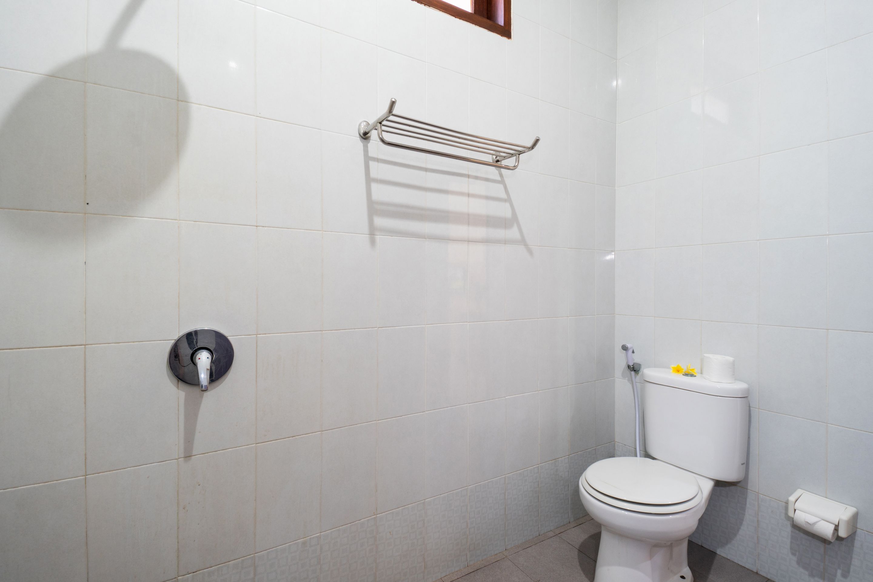 Un baño con azulejos blancos, inodoro, toallero y dispensador de papel higiénico.