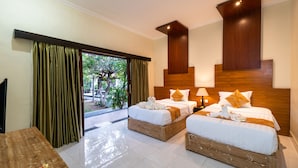 A hotel room with two beds, a wooden headboard, a wooden bench, and a view of greenery outside. - Pondok Jenggala (Lembongan Island)