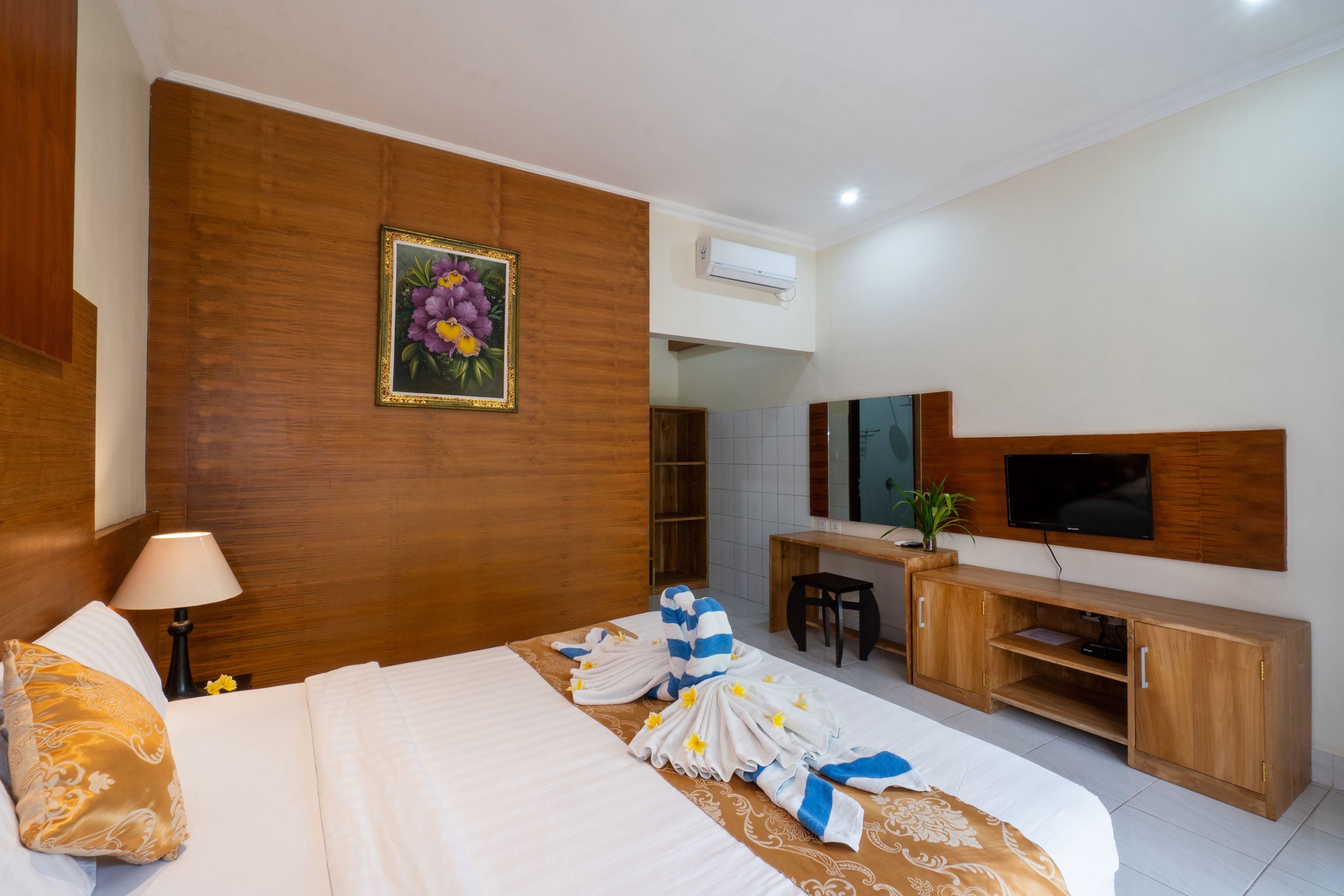 A hotel room with a bed, a wooden headboard, a television, a desk, and a plant.