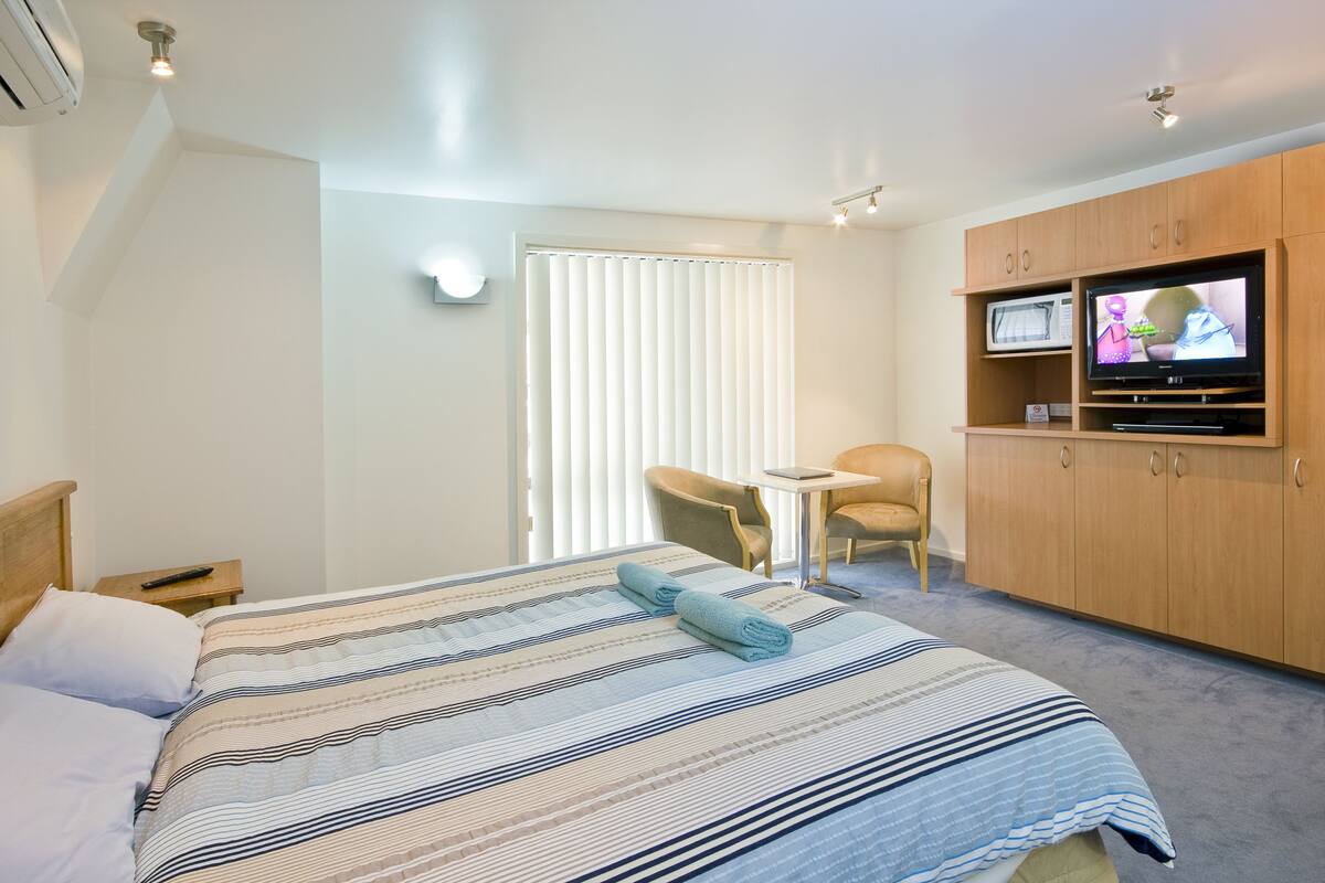 A hotel room with a bed, a TV, a chair, and a desk.