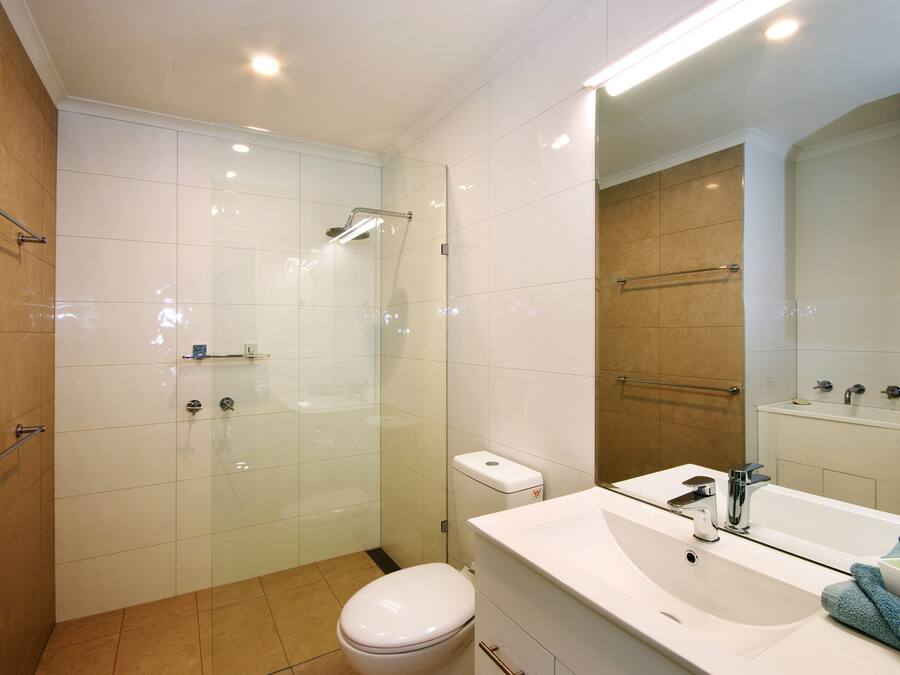 Un baño moderno con ducha envuelta en cristal, inodoro blanco y un espejo grande sobre un lavabo con toallero.
