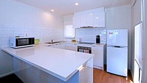 A modern kitchen with white cabinetry, a microwave, a coffee maker, and a refrigerator. - Anchorage Motel and Villas (Lorne)