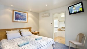 A hotel room with a bed, a television, a framed picture, and a bathroom visible through an open door. - Anchorage Motel and Villas (Lorne)