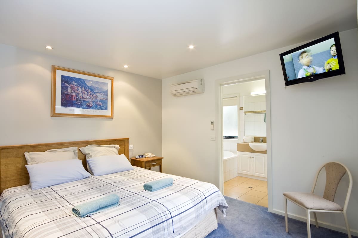 A hotel room with a bed, a television, a framed picture, and a bathroom visible through an open door.