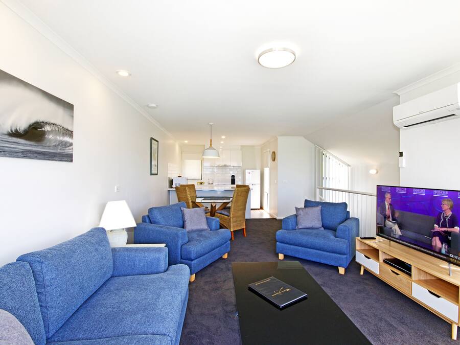 A modern living room with two blue sofas, a coffee table, and a flat-screen TV.