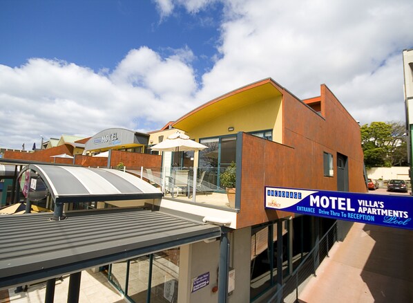 A modern motel with a yellow facade, a covered outdoor seating area, and a sign indicating a vacancy. - Anchorage Motel and Villas (Lorne)