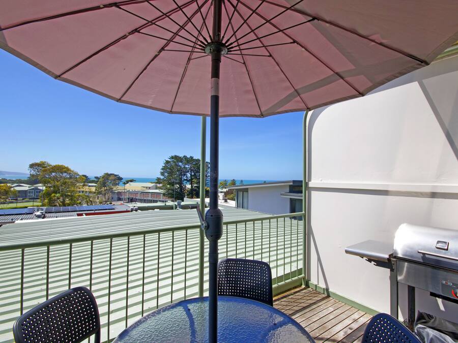 A balcony with a table, chairs, a grill, and an umbrella.