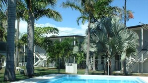 A swimming pool surrounded by palm trees and a fenced area with a building in the background. - Ocean Breeze Units (Bowen)