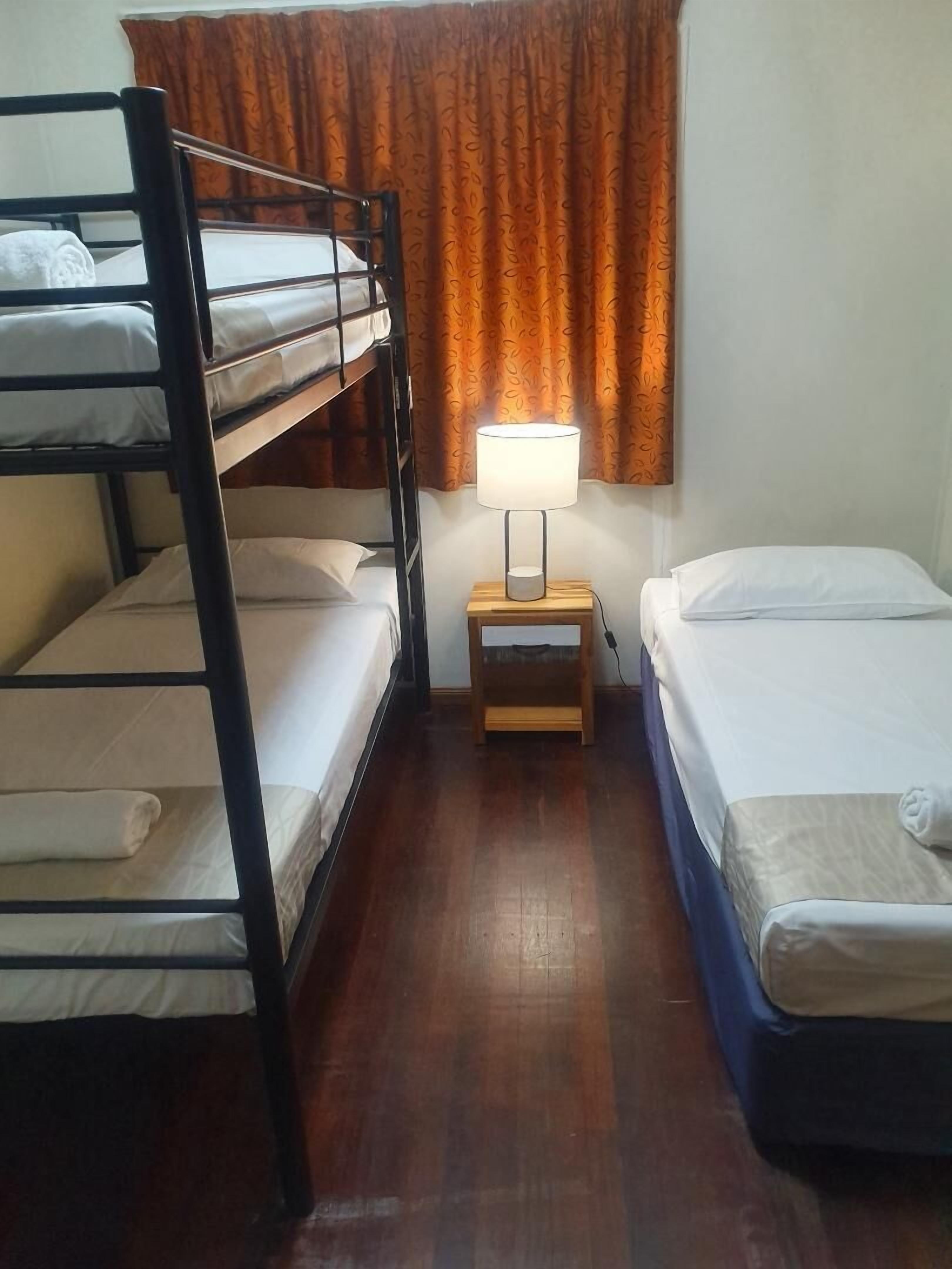 A room with bunk beds, a bedside table with a lamp, and a window with curtains.