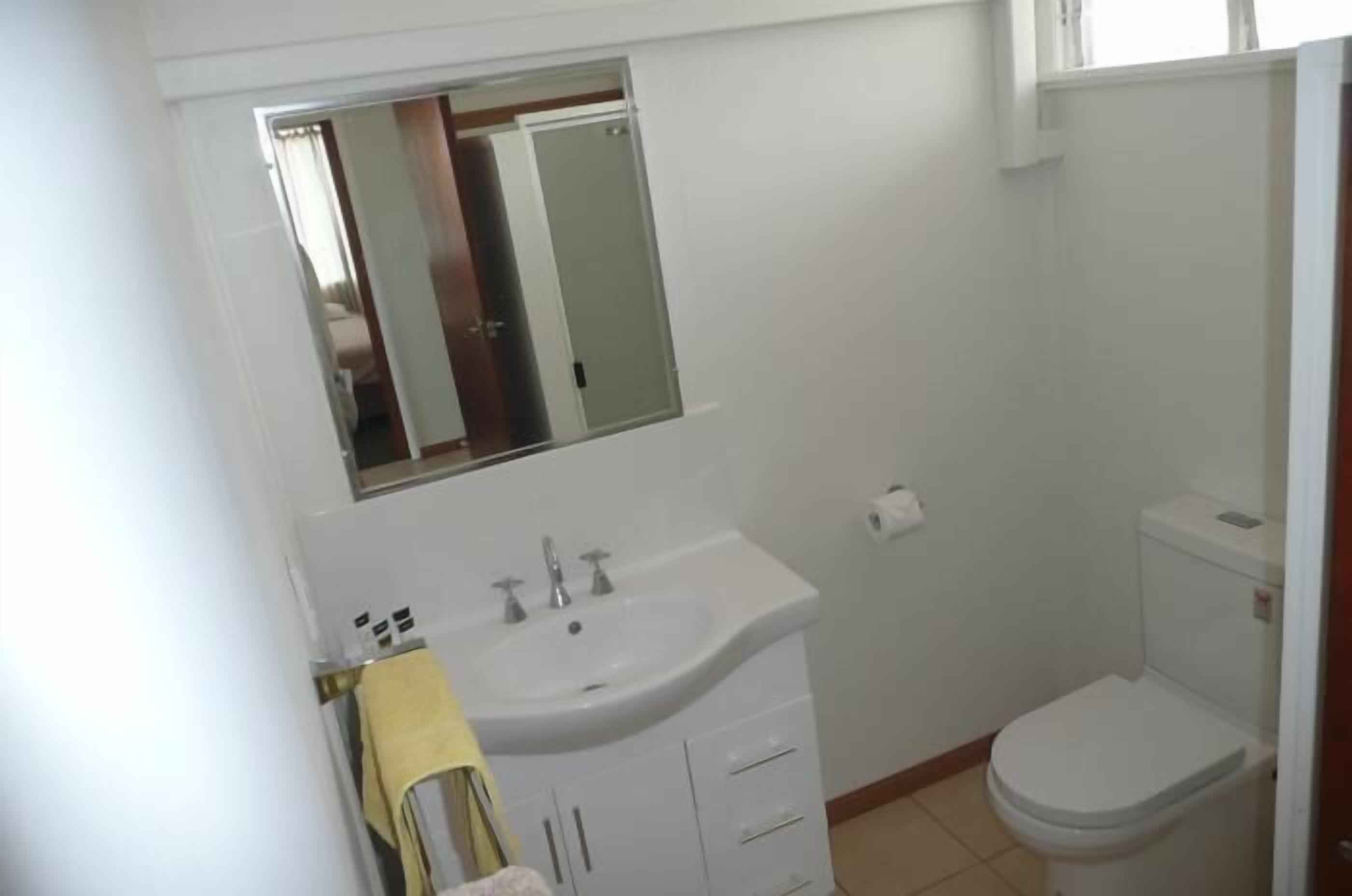 A small, clean bathroom with a white sink, mirror, and toilet.
