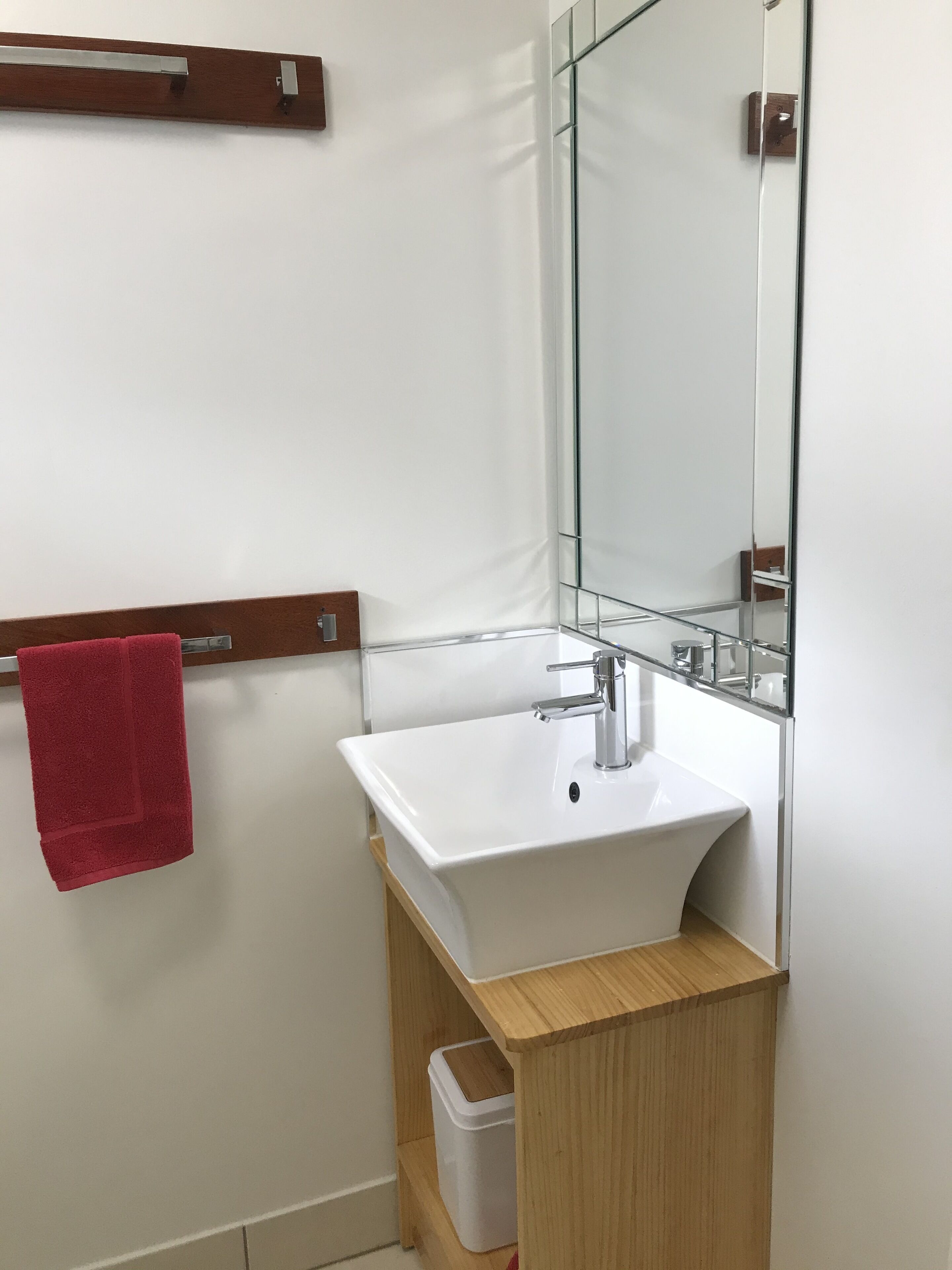 Une salle de bain avec un lavabo blanc, un miroir et une serviette rouge accrochée à un porte-serviettes.