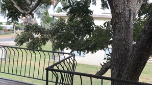 A wooden deck with metal railings, a tree, and a building in the background. - Ocean Breeze Units (Bowen)