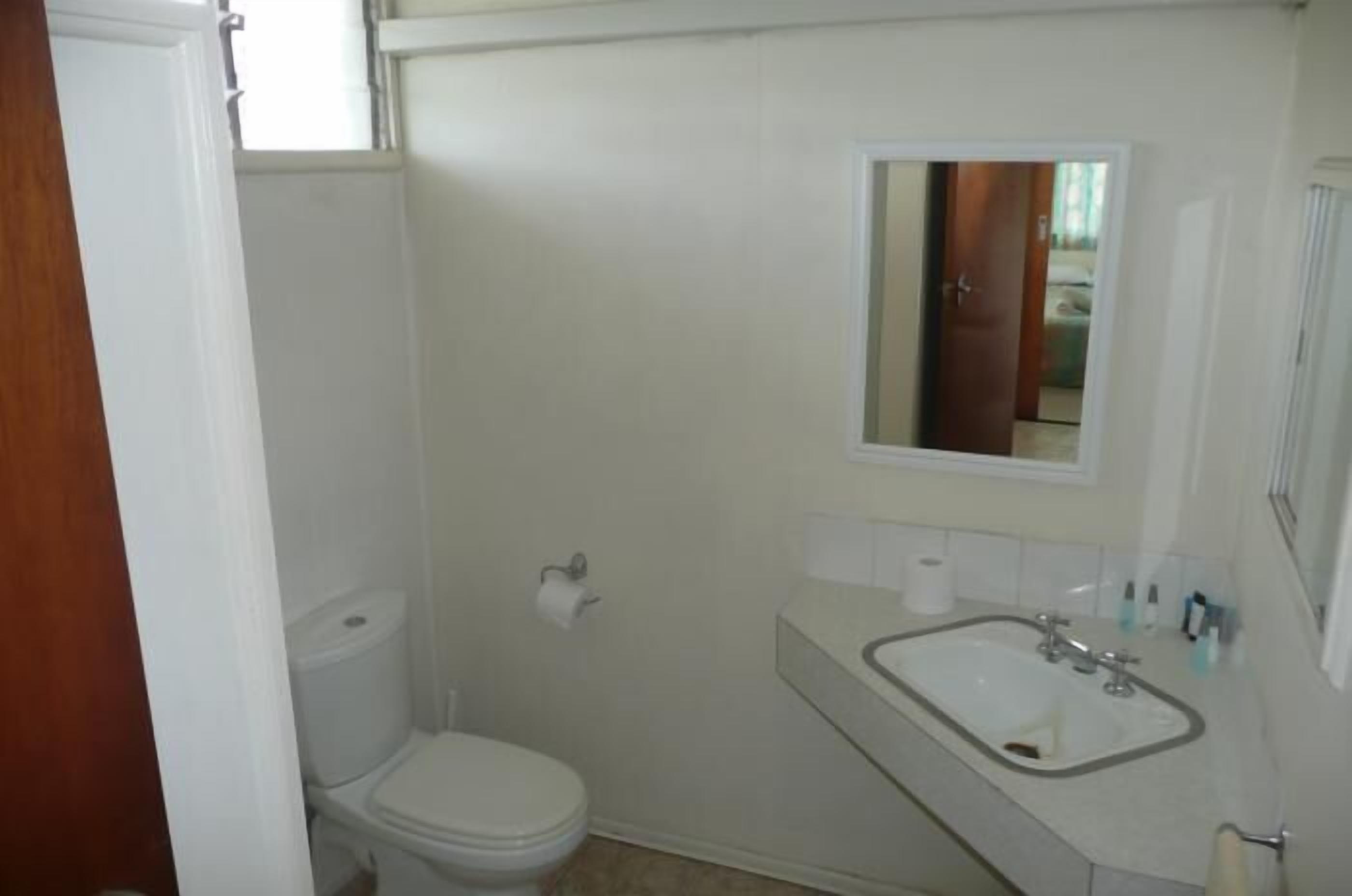 A small, white bathroom with a toilet, sink, and mirror.
