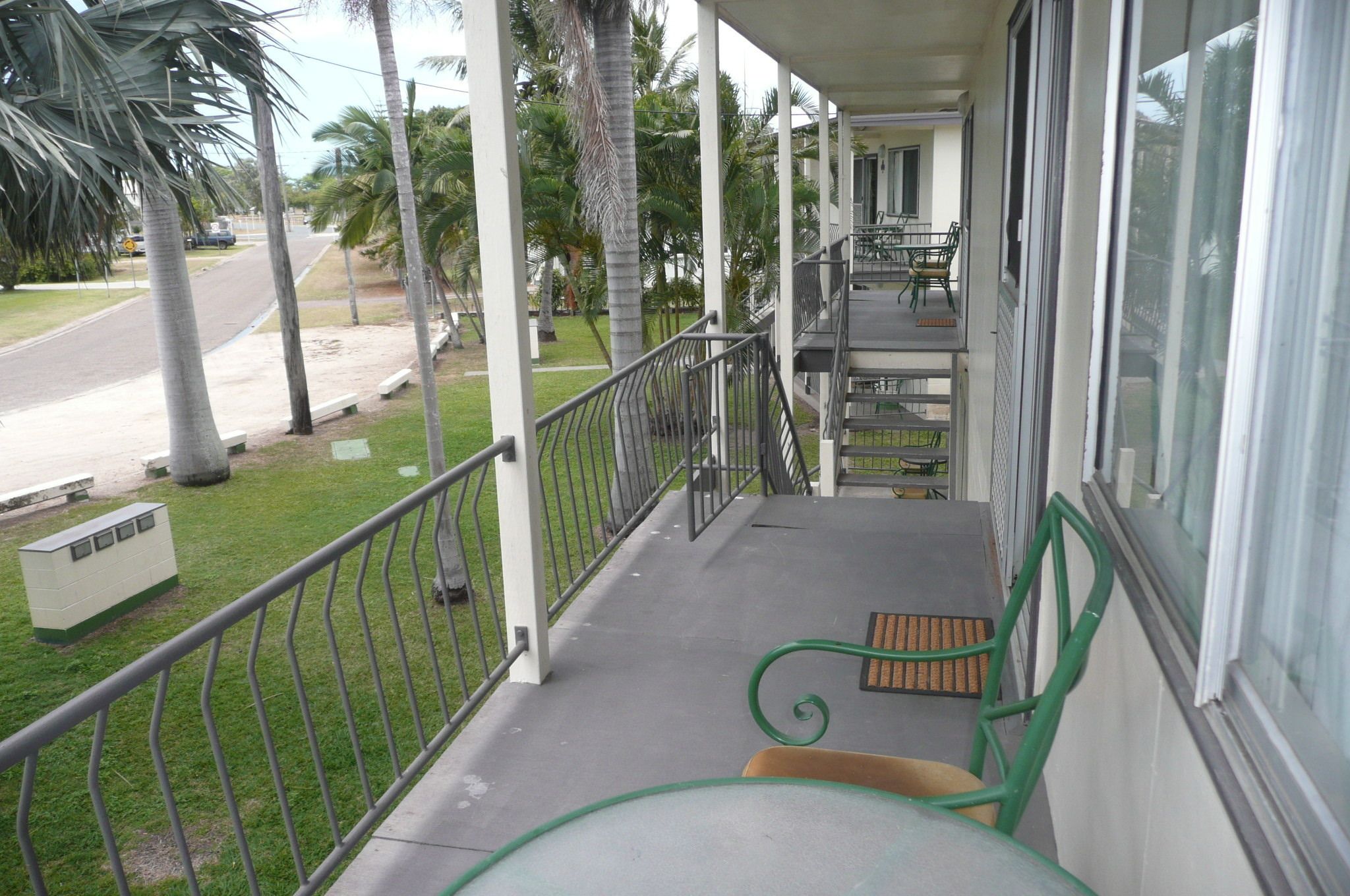 A covered outdoor area with a concrete floor, metal railing, and a few chairs.
