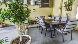 A covered outdoor dining area with a table and chairs, surrounded by potted plants and a large tree. - Golden Guitar Motor Inn (Hillvue)
