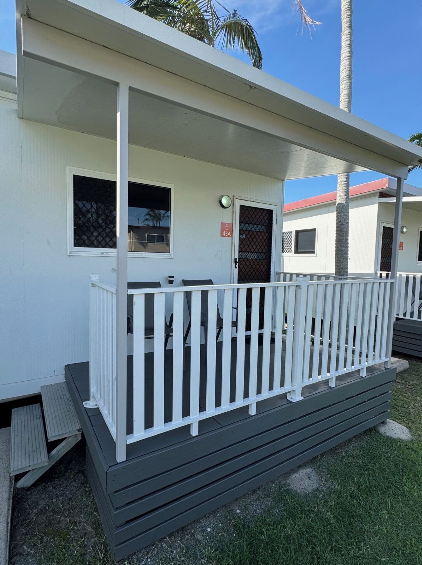 A single-story mobile home with a white exterior, a covered porch with white railings, and a small front deck.