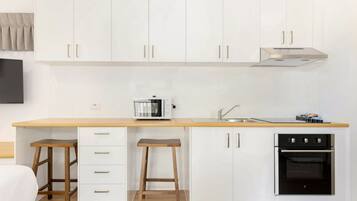 A compact kitchen with white cabinets, a microwave, a stove, and two stools.