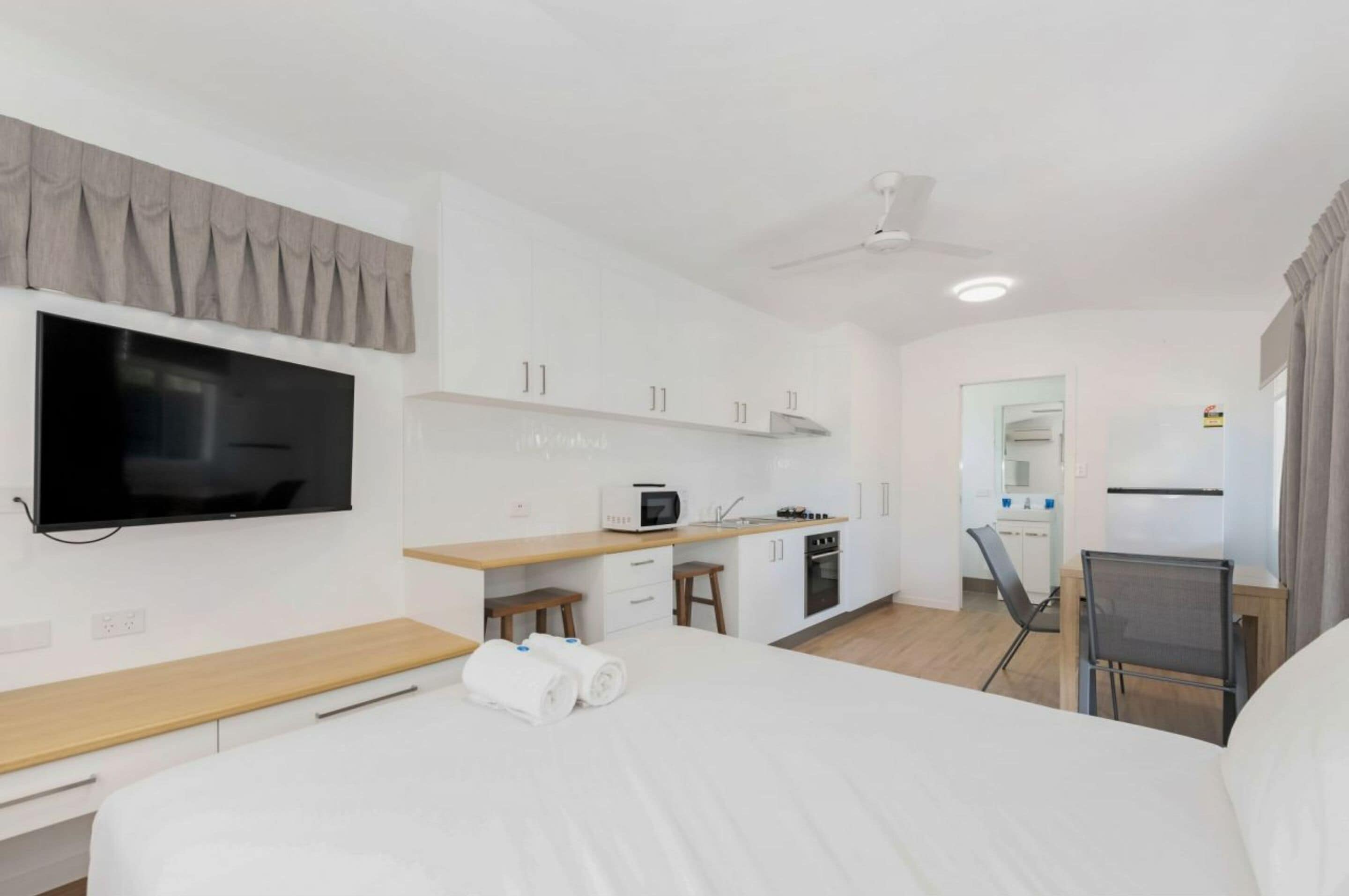 A modern hotel room with a bed, a TV, a kitchenette, and a seating area.