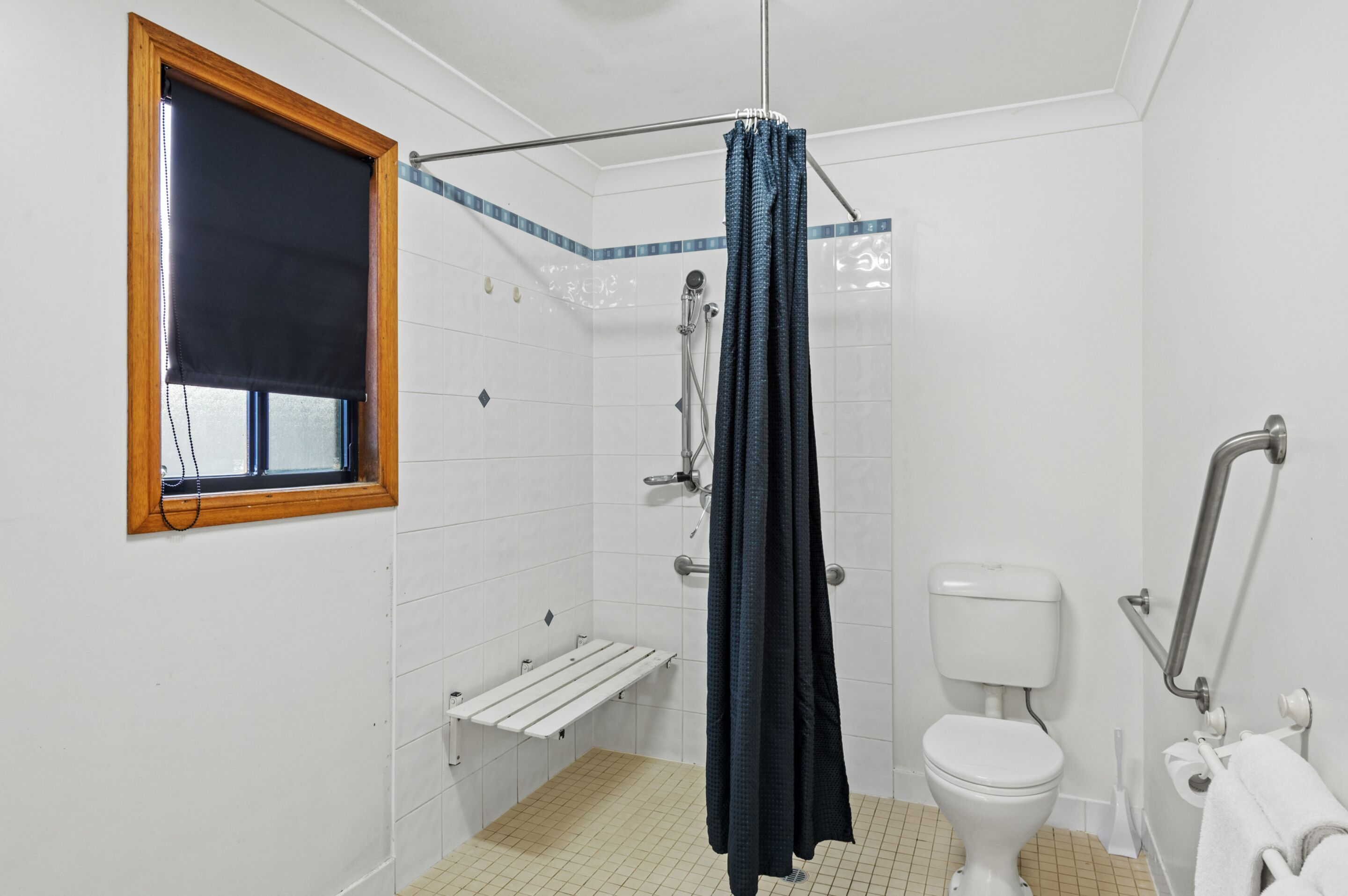 A bathroom with a shower, toilet, and a window with a blind.