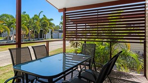 Un espacio de estar al aire libre cubierto con una mesa y sillas de vidrio, rodeado de palmeras y vistas a la calle.