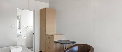 A bedroom with a bed, a desk, a chair, a wardrobe, and an air conditioning unit.
