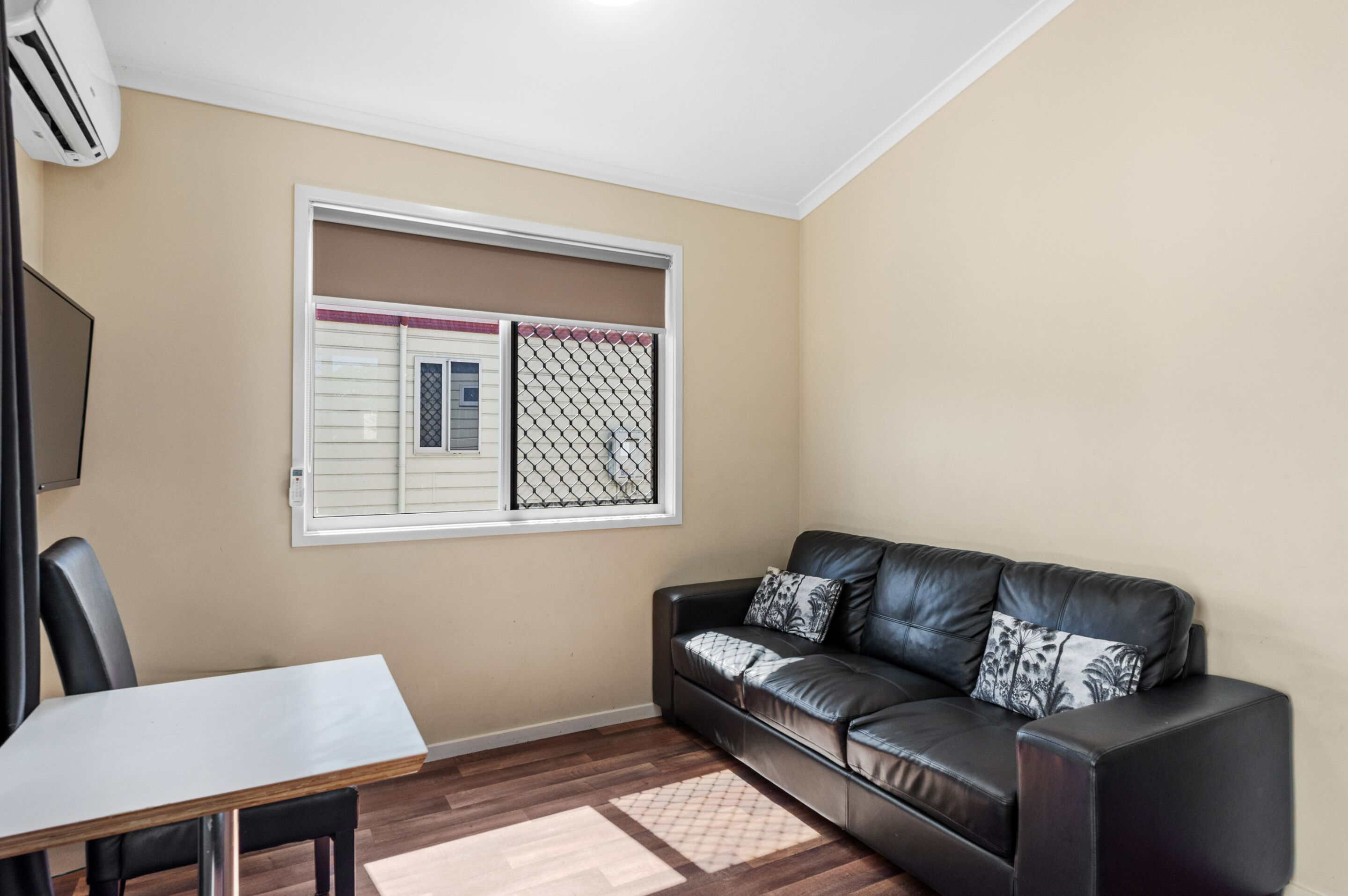 A living room with a black leather sofa, a white table, and a window with a metal screen.