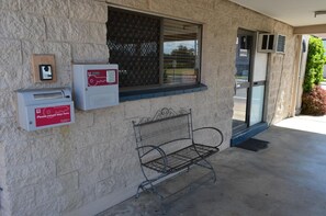 Un bâtiment avec un banc en métal, une boîte aux lettres et une fenêtre munie d’une grille en métal.