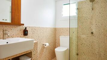Un baño con lavamanos blanco, inodoro y ducha con mampara de vidrio.