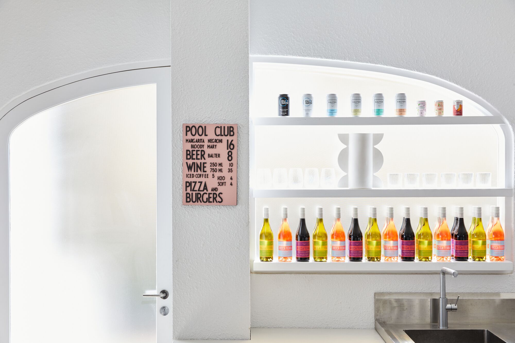 Zona de bar con un letrero que enumera bebidas y comidas, y botellas de refrescos en estantes.