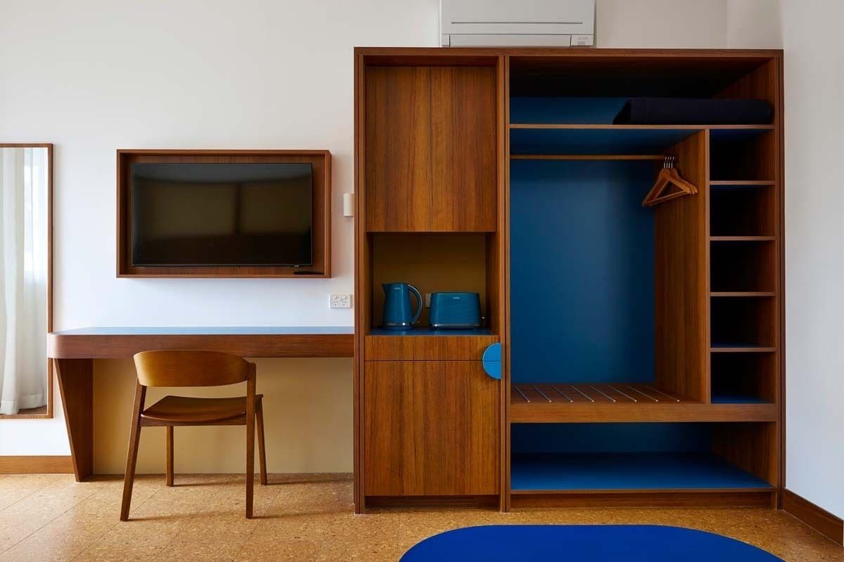 Quarto com escrivaninha de madeira, televisão, cadeira e guarda-roupa com prateleiras.