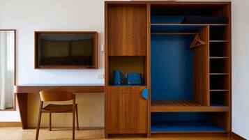 Quarto com escrivaninha de madeira, televisão, cadeira e guarda-roupa com prateleiras.