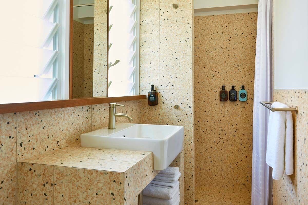 A bathroom with a sink, mirror, and shower area. There are towels and toiletries on the wall.
