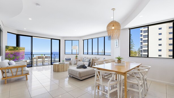 A modern living room with a dining area, large windows, and a view of the sea. - Meridian Alex Beach Apartments (Alexandra Headland)