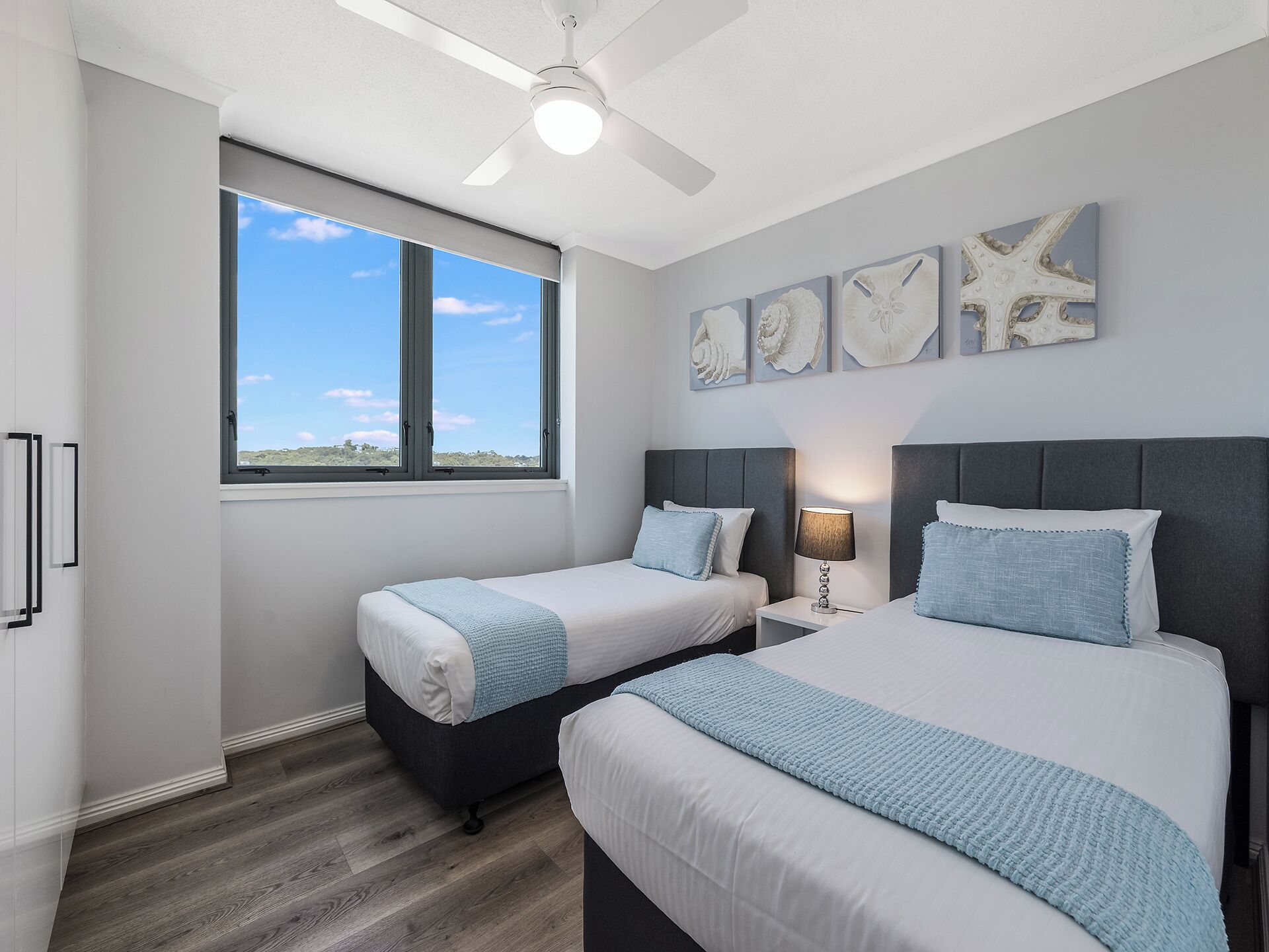 A bedroom with two beds, a ceiling fan, a window with a view, and wall art.