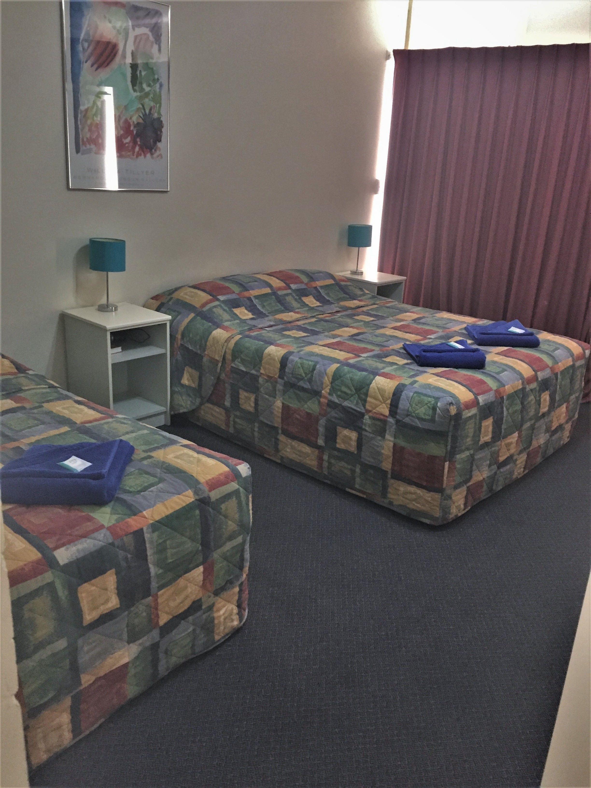 A hotel room with two beds, a small table, and a nightstand with lamps.