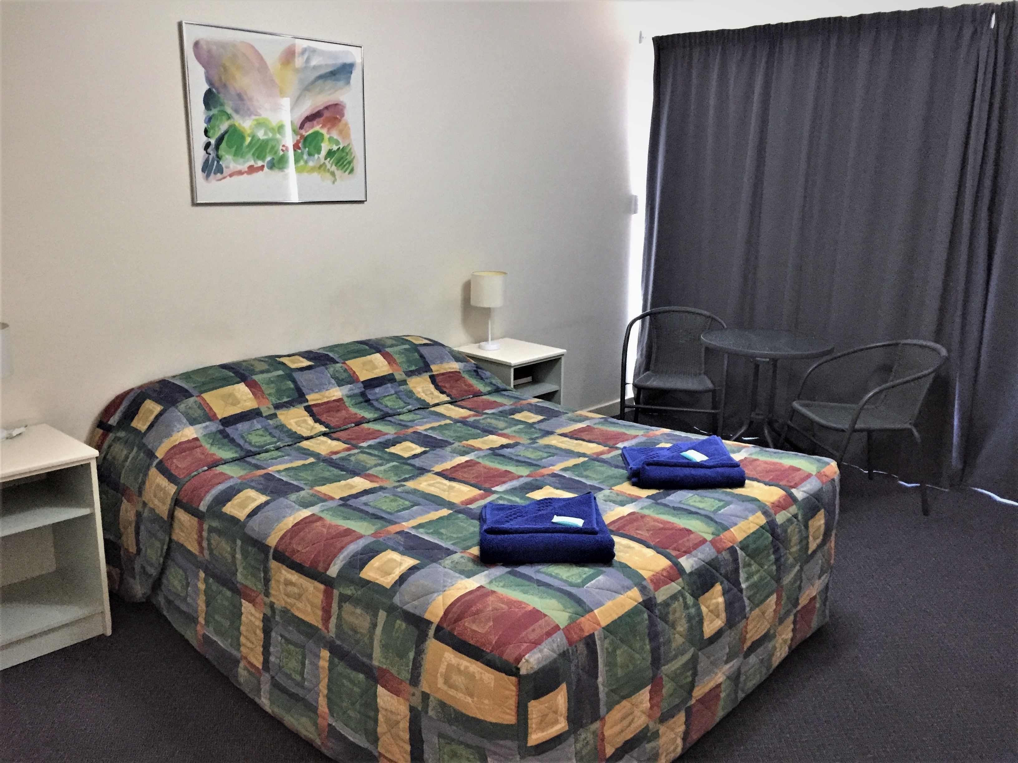Una habitación de hotel con una cama grande, una mesita, una silla y un cuadro en la pared.