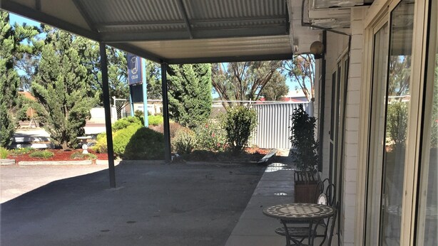 A covered outdoor area with a concrete floor, a small table with chairs, and a potted plant.