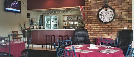 Un restaurante con pared de ladrillo, un reloj y una zona de bar con estantes llenos de botellas.
