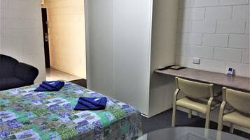 A hotel room with a bed, a desk, a chair, and a glass table.