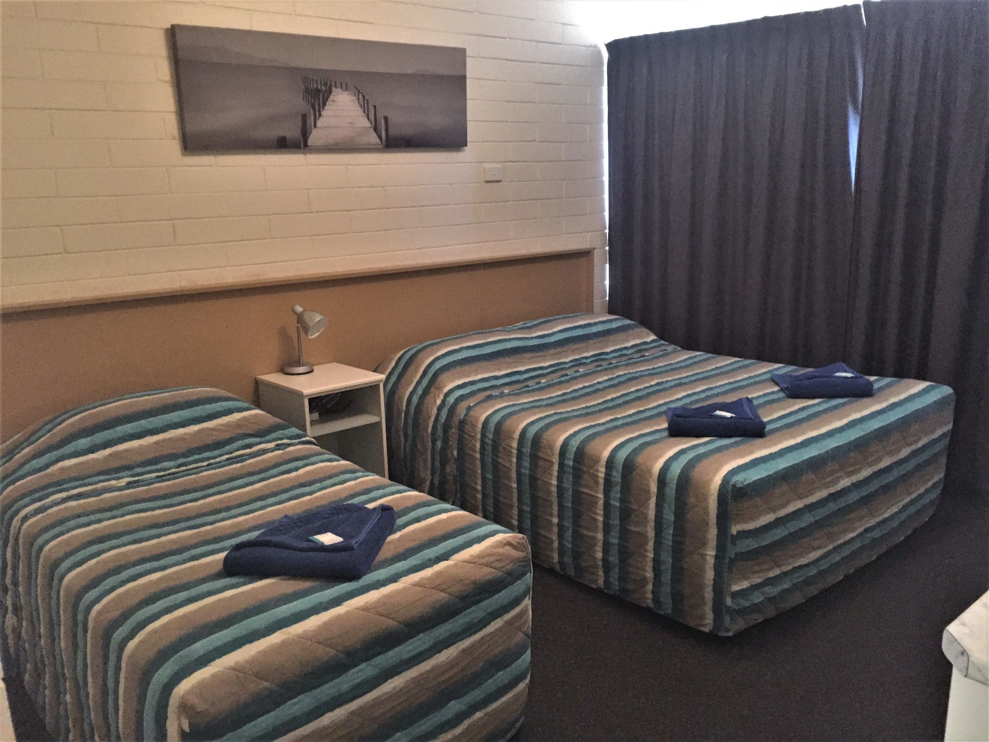 Ett hotellrum med två sängar, ett nattduksbord, en lampa och en tavla på väggen.