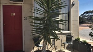 A building with a red door marked '26', a potted plant, outdoor chairs, and a gravel pathway. - Ceduna Motor Inn (Ceduna)