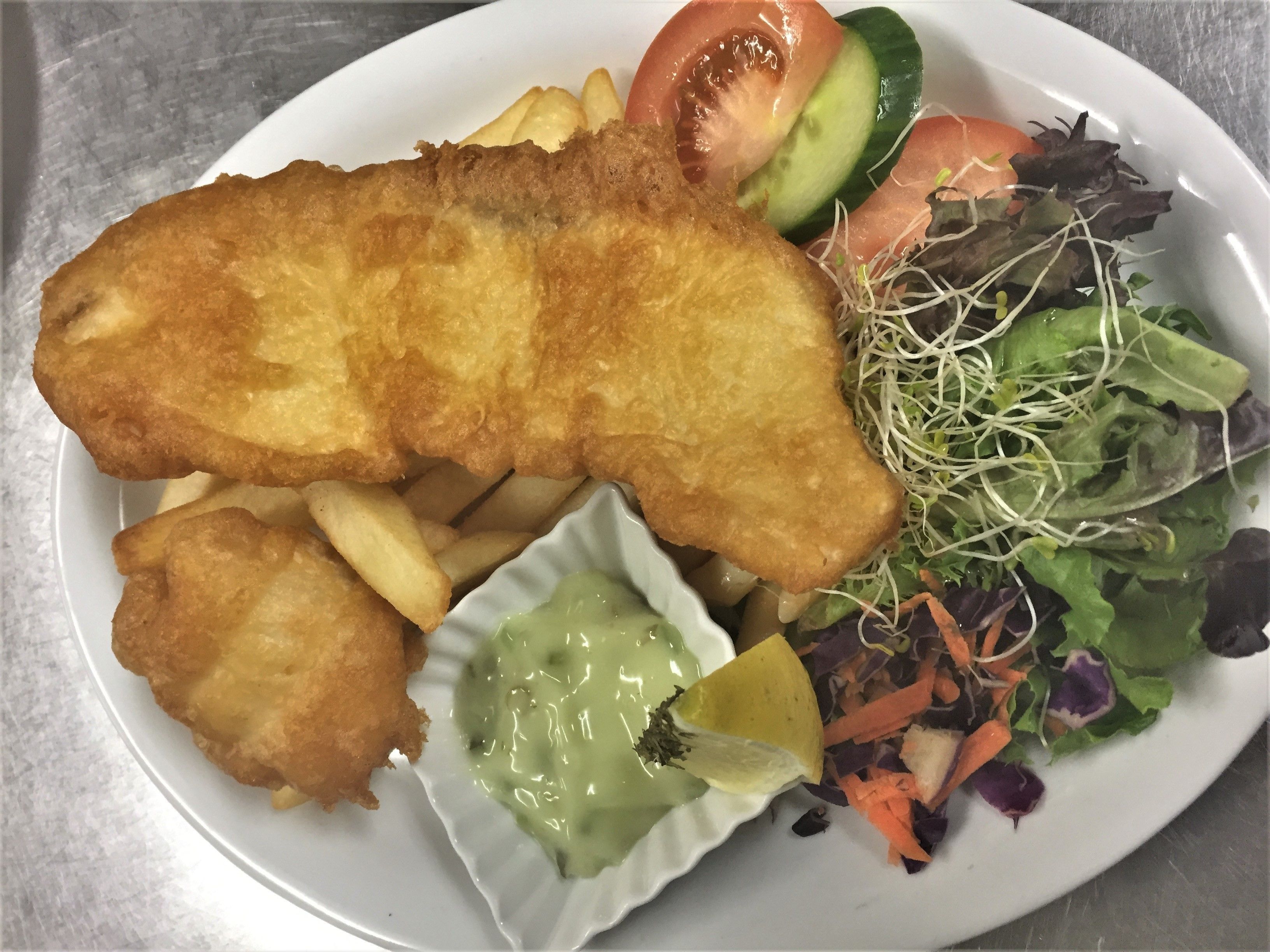 A plate with a breaded fish fillet, fries, a salad, and a small bowl of sauce.