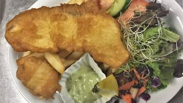 A plate with a breaded fish fillet, fries, a salad, and a small bowl of sauce.