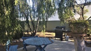 A patio with a round table and blue chairs, a barbecue grill, and a potted plant.