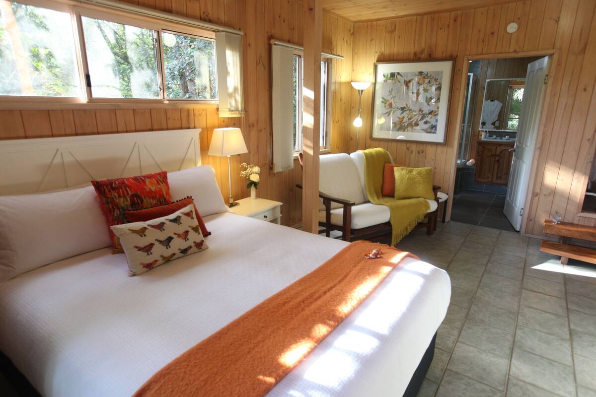A wooden-paneled bedroom with a large bed, bedside tables, a chair, and a view of a bathroom.